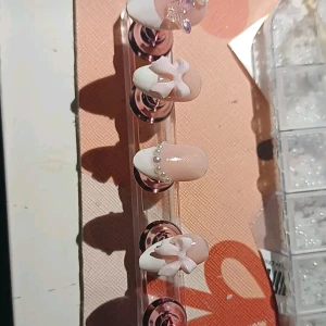 Rosa naglar med pärldetaljer - Snygga rosa lösnaglar med vita rosetter och pärldetaljer. Perfekt för en elegant look med en touch av glamour. Naglarna har en glittrig finish som ger extra bling.