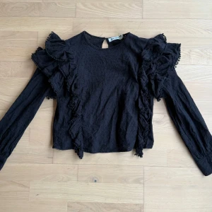 Svart blus från Carin Wester - Säljer en elegant svart blus från Carin Wester med volangdetaljer och långärmad design. Perfekt för att ge en stilfull touch till din outfit. Blusen har en rund hals och är tillverkad i ett lätt material. Storlek 34 💗