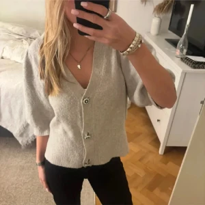 Beige kofta med knappar - Säljer en stilren beige kofta med knappar framtill. Koftan har trekvartsärmar och en v-ringad design. Perfekt för en avslappnad look.