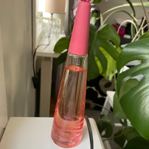 Rose & Rose Eau de Parfum - Elegant parfymflaska med en smal, avsmalnande design. Flaskan är genomskinlig med en rosa ton och har en rosa kork. Texten 'ROSE & ROSE' pryder framsidan. Perfekt för den som älskar blommiga dofter. Issey Miyake L'Eau D'Issey Rose & Rose Eau de Parfum Intense 90ml Spray