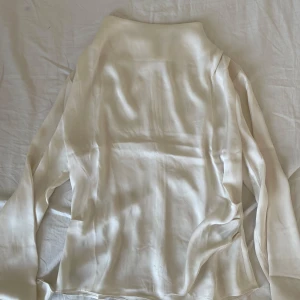 Vit satin blus  - Elegant vit blus i siden med långa ärmar. Perfekt för en stilren look. Blusen har en mjuk och glansig yta som ger en lyxig känsla.