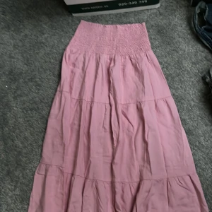 Rosa långkjol - Säljer en söt rosa långkjol med smockdetalj i midjan. Kjolen är perfekt för en avslappnad stil och har en luftig passform.