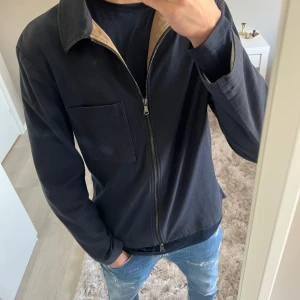 Mörklblå  jacka från J.Lindeberg - Säljer en stilren mörklblå  jacka från J.Lindeberg. Jackan har en dragkedja framtill och en bröstficka. Perfekt för en casual look och passar bra till jeans. Ny pris 2600 mitt pris 1900