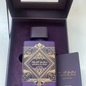 Lattafa Badee Al Oud Amethyst   - Elegant parfymflaska i en djup lila nyans med guldiga detaljer och geometriskt mönster. Doften heter Badee Al Oud Amethyst och kommer i en lyxig förpackning. Perfekt för den som älskar orientaliska och träiga dofter. Mer än 90 ml kvar.