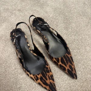 Leopardmönstrade pumps från Mango - Snygga pumps från Mango med spetsig tå och leopardmönster i bruna och svarta toner. Skorna har smal klack och öppen häl med rem. Perfekta för dig som vill sticka ut med en trendig och djurinspirerad look.