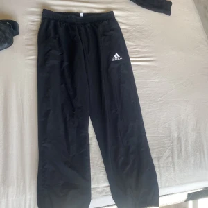 Svarta träningsbyxor från Adidas M - Svarta träningsbyxor från Adidas med vit logga på låret. Byxorna har elastisk midja och är tillverkade i lätt, återvunnet Primegreen-material med meshfoder. Perfekta för sport eller chill. Klassisk och enkel design.