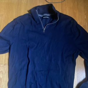 Marinblå half zip tröja Jack & Jones - Snygg marinblå långärmad tröja från Jack & Jones med half zip-dragkedja i halsen. Tröjan har en stilren design och är gjord i mjuk bomull, perfekt för chill dagar eller när du vill se casual ut. Passar dig som gillar enkel och clean stil.