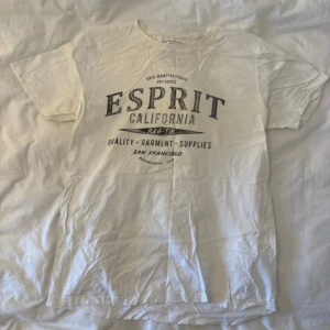 Vit Esprit t-shirt med tryck - Vit t-shirt från Esprit med stort svart tryck på bröstet där det står 'Esprit California'. Rund hals och korta ärmar. Mjuk bomullskvalitet och klassisk passform. Perfekt för chill dagar och enkel att matcha med jeans eller shorts.