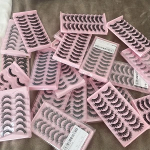 Falska ögonfransar i volymstil - Säljer flera paket med volymiga falska ögonfransar i svart, förpackade i rosa plastaskar. Fransarna har en fyllig och böjd form som ger en dramatisk look. Perfekt för dig som vill ha extra långa och täta fransar. Materialet är syntetiskt och varje ask innehåller flera par.