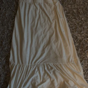 Vit långkjol från JDY - Säljer en vit långkjol från JDY i storlek L. Kjolen har broderade hål och volangdetalj nedtill som ger en chill och romantisk vibe. Perfekt för varma dagar och har en luftig passform. Materialet känns mjukt och är troligtvis bomull.