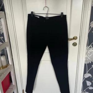 Svarta slim kostymbyxor Jack & Jones - Svarta kostymbyxor från Jack & Jones, modell Slim/Marco. Byxorna har en smal passform, klassiska fickor fram och bak samt bälteshällor. Perfekta för en clean och stilren look. Materialet är mjukt och följsamt, vilket gör dem riktigt bekväma.