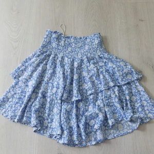 Blåvit blommig volangkjol - Supersöt kort kjol med blått och vitt blommönster och flera volanger. Köpte på ullared förra året, har inte kommit till någon användning💞