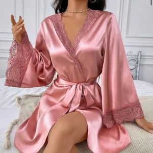 Rosa omlottklänning i satin med spets - Supersnygg kort rosa omlottklänning i satin med breda ärmar och spetsdetaljer vid halsringning och ärmslut. Använda inte och har inget nytta av den, den är dock i topp skick! Skriv gärna för fler bilder💕😊