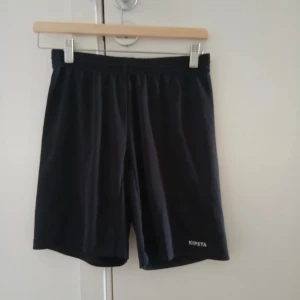Svarta träningsshorts från Kipsta - Svarta shorts från Kipsta med elastisk midja och snörning för perfekt passform. Barnstorlek 164 