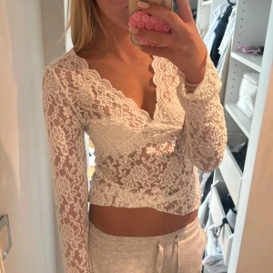 Vit spetsblus med v-ringning - Superfin vit blus i spets med v-ringad hals och långa ärmar. Blusen är genombruten med blommigt spetsmönster och har en feminin, figurnära passform. Perfekt för dig som vill ha en romantisk och trendig look.