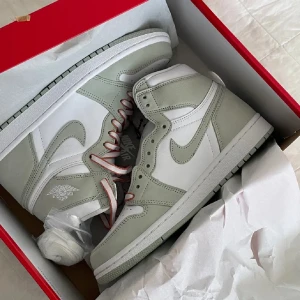 Nike Air jordan 1 High OG Seafoam  - Ett par Nike Air jordans i ljusgrön mocka och vitt läder köpta här på plick. De två första bilderna är den förra säljarens. Den sista bilden är hur de ser ut nu. Dem är i storlek 39 med vita och oranga skosnören utöver de gröna som är på nu! De är använda ett par gånger och har gångstreck men annars är de i bra skick. Kontakta för mer bilder. 