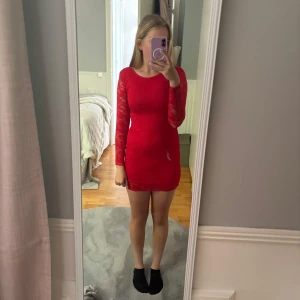 Röd klänning - Snygg röd spetsklänning från Cubus med långärmade spetsdetaljer och rund hals. Klänningen har en tight passform och rygg med knappstängning. 