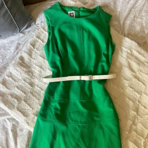 Grön kort klänning från Anne Klein - Snygg grön klänning från Anne Klein i kort modell med ärmlös design och rund hals. Klänningen har en vit bälte i midjan som går att ta bort och dragkedja bak. Super fint skick utan defekter! Nypris ligger på 150 dollar. Storlek 2 i amerikanskt mått men 34 i EU storlek. 