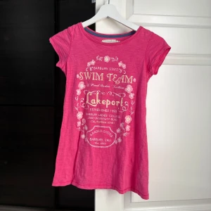 Rosa topp med tryck  - Snygg rosa t-shirt från H&M med text och blommigt tryck framtill. Modellen har rund halsringning och korta ärmar.