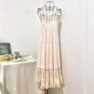 Ljusrosa långklänning med spetsdetaljer - Romantisk ljusrosa långklänning med tunna axelband och v-ringad spets upptill. Är lika genomskinlig som du ser i bilden (mer transparent vid brösten än på nedre delen). Storlek XS-S (34-36). Dockans storlek: 34.