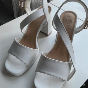 Vita klackskor med klack  - Snygga vita klackskor med breda remmar och chunky klack. Skorna har öppen tå och en cool guldfärgad spänndetalj vid ankeln. Tillverkade i syntetmaterial med en stilren och modern look som passar perfekt till sommarens outfits. Endast använda en gång!