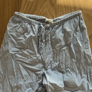 Randiga bomullsbyxor från H&M - Luftiga byxor från H&M i blåvitt randigt mönster. De har resår och snörning i midjan för skön passform. Perfekta för chill dagar eller när du vill ha något bekvämt. Tillverkade i tunn bomull som andas.