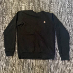 Svart sweatshirt från Dickies XS - Svart sweatshirt från Dickies i storlek XS. Klassisk crewneck med liten Dickies-logga på bröstet. Tröjan har långa ärmar och ribbade muddar vid hals, ärmslut och nederkant, och ett pyttelitet hål på högra ärmen (sista bilden med en tia som referens)Tveka inte med att höra av dig vid prisförslag eller annan fundering!