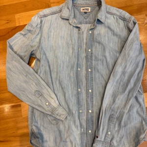 Ljusblå jeansskjorta Hilfiger Denim M - Snygg ljusblå jeansskjorta från Hilfiger Denim i storlek M. Skjortan har klassisk krage, långa ärmar och knappar framtill. Tillverkad i mjukt jeanstyg med diskreta sömdetaljer och liten logga vid ärmslutet. Perfekt för en avslappnad och cool stil.