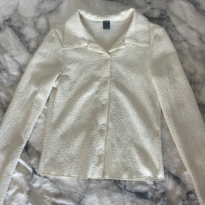 Vit texturerad skjorta från SHEIN - Snygg vit skjorta från SHEIN i storlek S med lång ärm och klassisk krage. Skjortan har en skimrande, texturerad yta och knäpps framtill med vita knappar. Materialet känns lätt och har en subtil glans som ger en cool look. Skjortan kom ej till användning!