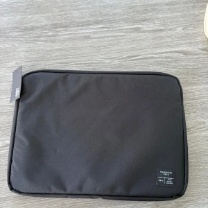 Svart datorväska 15 tum - Minimalistisk svart datorväska från lager157, passar 15-tums laptop. Tillverkad i slitstark polyester med enkel design och diskret etikett på framsidan. Perfekt för att skydda din dator på språng.