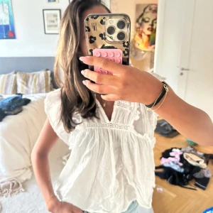 Vit blus med volang från Neo Noir❣️ - Supersöt vit blus från Neo Noir med volangdetaljer längs ärmar och axlar. Blusen har v-ringning, broderade partier och är tillverkad i ett lätt och luftigt bomullstyg. Så söt och passar till allt!😍