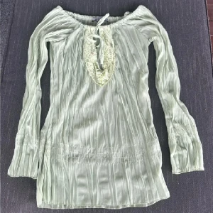 Ljusgrön blus med spets och knyt - Supersöt ljusgrön blus i tunn, plisserad polyester med långa ärmar. Djup v-ringning med spetskant och paljettdetaljer, samt knytband framtill. Sitter offshoulder och har en flowy, romantisk vibe. Perfekt för dig som gillar unika detaljer och boho-stil. Vintage❤️