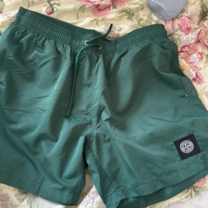 Gröna badshorts från Stone Island  - Snygga gröna badshorts från Stone Island med klassisk logopatch på benet. Shortsen har elastisk midja med snörning, innerbyxa i mesh och praktisk bakficka med lock. Perfekta för sommaren och strandhäng. Obs storlek XL men dem är små o storlek för jag har tvättat använt dem så dem passar M nu. Äkta såklart med