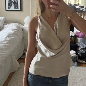 Beige omlott linnetopp med rosett - Säljer en beige topp i glansigt satinliknande material. Den är väldigt skön att ha på sig och du kan ha den på flera olika sätt, vilket gör att du kan bära den flera gånger men ändå inte se exakt lika dan ut 😇💓💓