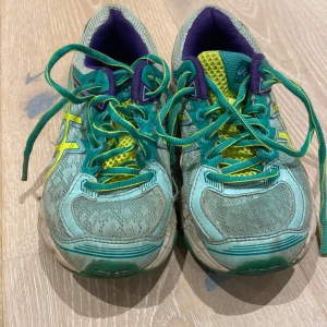 Turkosa Asics sneakers med gula detaljer - Snygga Asics sneakers i turkos mesh med gula och lila detaljer. Skorna har snörning, rund tå och platt sula. Ovandelen är i syntet och skinn, sulan i gummi. Perfekta för dig som gillar färg och sportig stil.