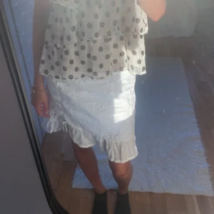 Vit kortkjol med volang från H&M - Supersöt vit kortkjol från H&M med broderade blommor och volangkant längst ner. Kjolen är gjord i mjuk bomull och har en normal passform med resår i midjan. Perfekt för sommarens alla dagar, matcha med din favorit-topp för en fräsch look.