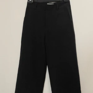 Svarta kostymbyxor från Madlady - Svarta kostymbyxor från Madlady med raka ben och midjehällor. Klassisk design med fickor framtill och diskret dragkedja. 