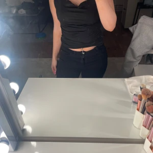 Svart croppad linnetopp - Säljer en svart croppad linnetopp med smala axelband och figurnära passform. Toppen har en enkel och stilren look som passar perfekt till jeans eller kjol. Materialet känns mjukt och följsamt mot kroppen. Perfekt för dig som gillar minimalistisk stil.