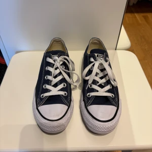 Mörkblå Converse All Star sneakers - Klassiska Converse All Star sneakers i mörkblå canvas med vita gummisulor och tåhättor. Skorna har vita snören, silverfärgade öljetter och tydliga kontrastsömmar. Använt fåtal gånger. Lite slitna på det vita tåhättorna men det framgår på sista bilden.