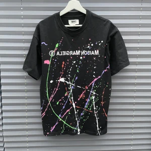Maison Margiela T-shirt - Svart t-shirt från Maison Margiela med coola färgstänk i grönt, rosa, vitt, lila och rött. Med ett Maison margiela tryck på bröstet med. T-shirten är knappt använd och är i väldigt bra skick. Bara höra av er vid minsta fråga eller fundering!