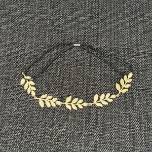 Guldigt hårband med bladmotiv - Unikt hårband med guldfärgade blad i metall, sammankopplade på en tunn svart snodd. Bladen har fina detaljer och ger en bohemisk och trendig känsla. Perfekt accessoar för att lyfta din outfit med en touch av naturinspiration.