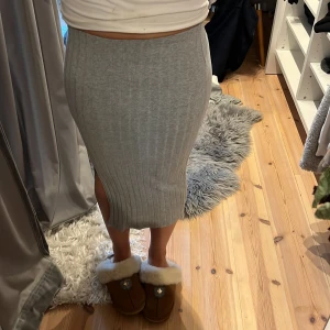 Grå ribbad långkjol med slits - Säljer en snygg grå långkjol med ribbad struktur och slits på sidan. Kjolen har en tight passform  och är gjord i ett stickat material som känns mjukt och skönt mot huden. Perfekt för dig som gillar stilrena och enkla plagg.