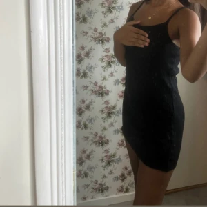 Svart ribbad kort klänning - Säljer en svart ribbad kortklänning med smala axelband och tight passform. Klänningen är ärmlös och har en enkel, stilren design som passar perfekt till sommaren. Materialet är stretchigt och bekvämt, vilket gör den lätt att bära hela dagen.