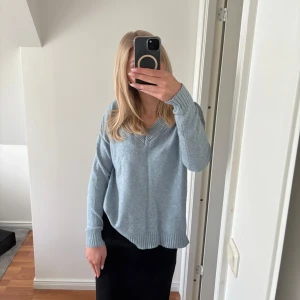 Ljusblå stickad v-ringad tröja - Mysig ljusblå stickad tröja med v-ringning och långa ärmar. Tröjan har ribbade muddar vid ärmslut och nederkant, perfekt för en avslappnad och stilren look.