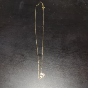 Guldfärgat halsband med hjärthänge - Säljer ett tunt guldfärgat halsband med ett litet hjärta som hänge. Perfekt för att ge en söt touch till din outfit. Kedjan är enkel och stilren, och hjärtat har en glittrig yta som fångar ljuset fint. Liten i storleken runt halsen