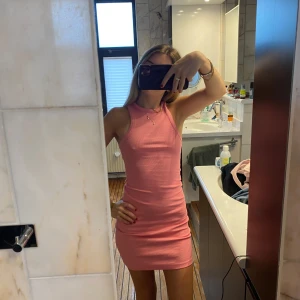 Rosa ribbad kortklänning - Säljer en söt rosa ribbad klänning med tight passform och ärmlös design. Klänningen är kort och har en enkel, stilren look som passar perfekt till sommaren. Perfekt för dig som gillar en feminin och trendig stil.