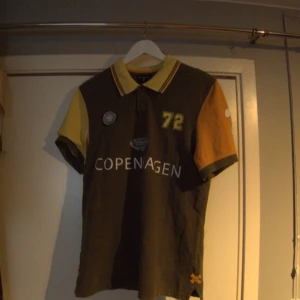 Pikétröja - Ascool mörkgrön, gul och orange pikétröja "Copenhagen International racetracks" som har många olika detaljer. Inga deffekter, står M men passar också som small.