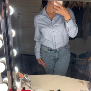 Blåvit randig skjorta - Snygg blåvit randig skjorta med klassisk krage och knäppning framtill. Skjortan har långa ärmar och är tillverkad i ett mjukt material. Perfekt att styla med jeans eller kjol för en clean look.