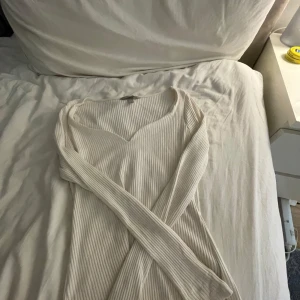 Vit ribbad långärmad tröja från H&M - Säljer en vit ribbad långärmad tröja från H&M. Tröjan har en v-ringad halsringning och är tillverkad i ett mjukt, stretchigt material som sitter skönt på kroppen. Perfekt att styla till jeans eller kjol. Jättebra skick, pris kan diskuteras!