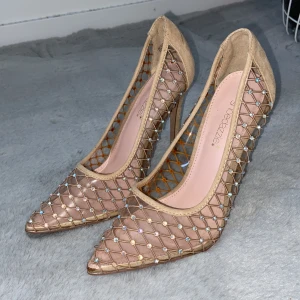 Beige pumps med nät och pärldetaljer - Säljer dessa glamorösa klackar från ShoeDazzle i storlek 38. De är endast testade hemma, men tyvärr är klacken lite för hög för mig (10 cm), så de har blivit stående i garderoben.  ✅ Storlek: 38 ✅ Klackhöjd: 10 cm ✅ Skick: I princip nya – endast testade ✅ Detalj: Liten, knappt synlig skavank på ena klacken (se bild) ✅ Stil: Eleganta med glittrande detaljer – perfekta för fest eller event  🌟 Skorna är bekväma i modellen men har en hög klack, så de passar bäst för dig som är van vid det!